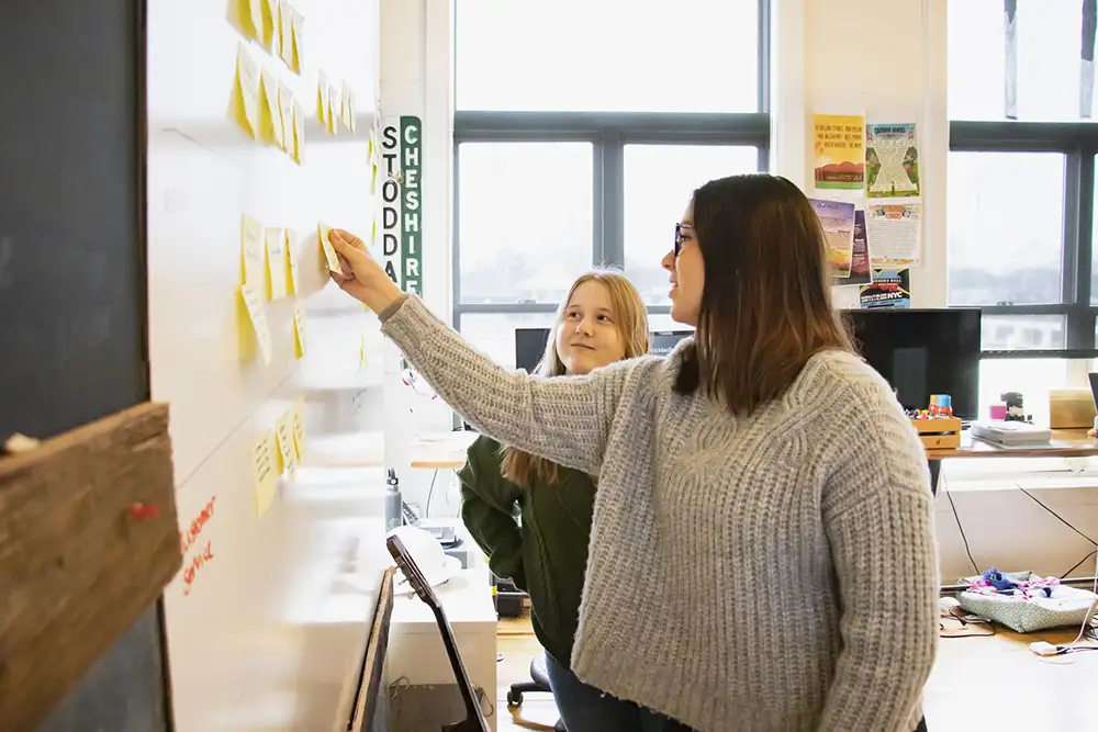 Two women moving sticky notes on a whiteboard in an office