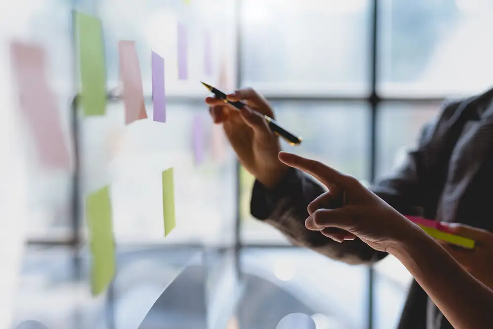 A close up of hands hovering next to sticky notes on a whiteboard