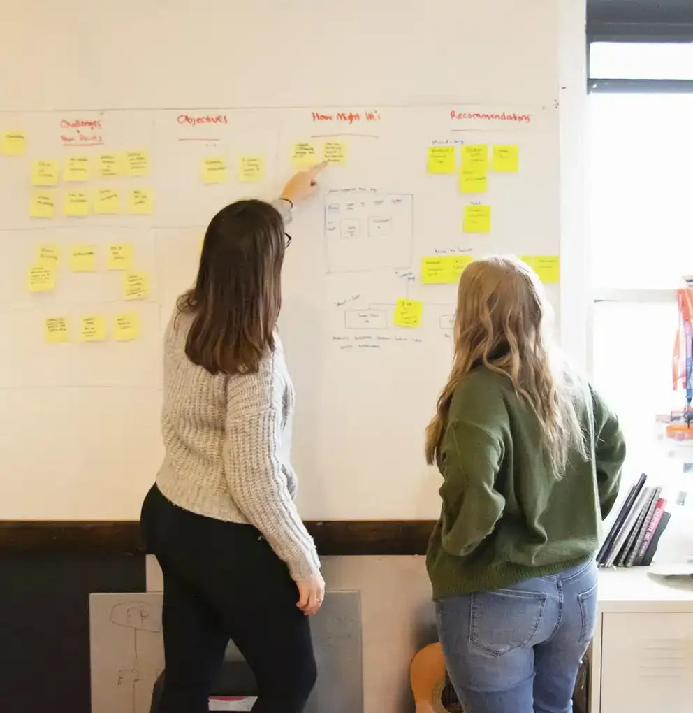 Heather and Hanna putting sticky notes on a whiteboard
